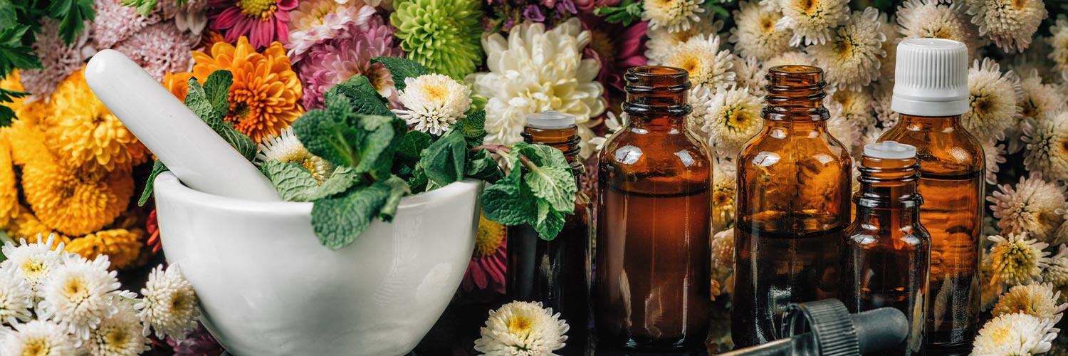 Bachblüten und Kräuter mit Mörser, Pipettenfläschchen und verschiedenen Blüten im Hintergrund.