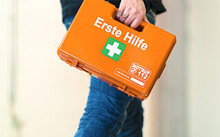 Eine Person trägt einen orangefarbenen Erste-Hilfe-Koffer mit weißem Kreuz.