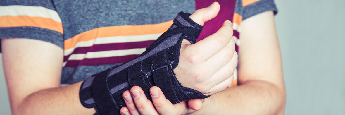 Eine Person trägt eine schwarze Handgelenkorthese und stützt den betroffenen Arm mit der anderen Hand.