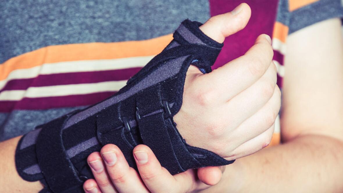 Eine Person trägt eine schwarze Handgelenkorthese und stützt den betroffenen Arm mit der anderen Hand.