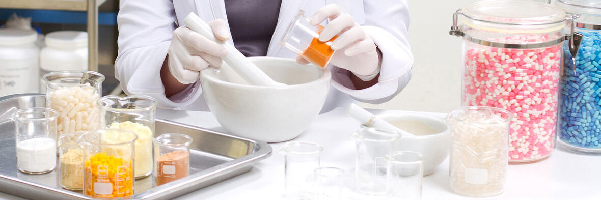 Eine Apothekerin stellt mit Mörser und verschiedenen Wirkstoffen eine individuelle Arzneimittelrezeptur her.