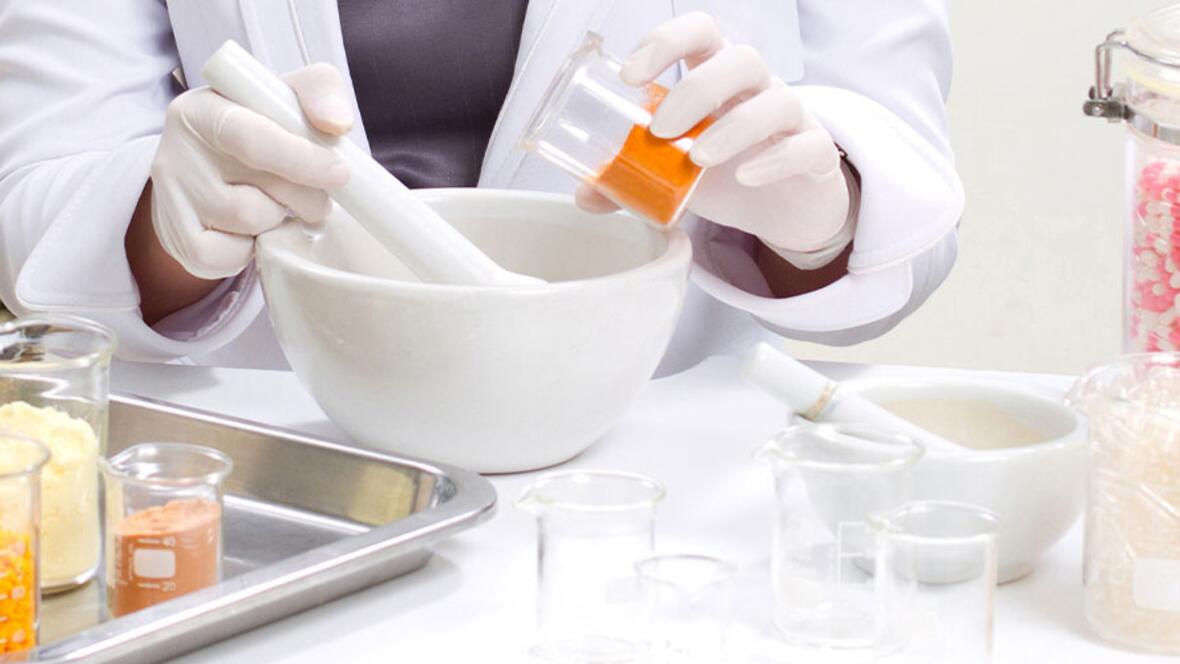Eine Apothekerin stellt mit Mörser und verschiedenen Wirkstoffen eine individuelle Arzneimittelrezeptur her.