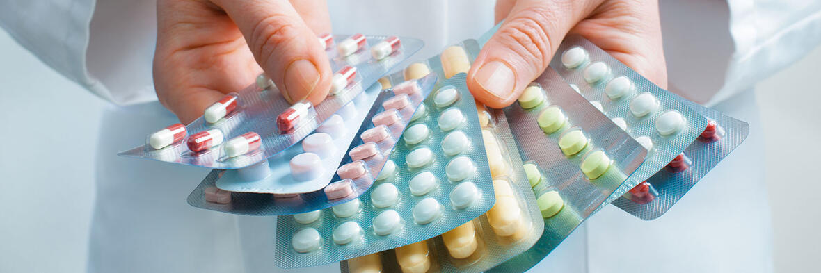 Eine Person hält mehrere Blisterpackungen mit verschiedenfarbigen Tabletten und Kapseln in den Händen.