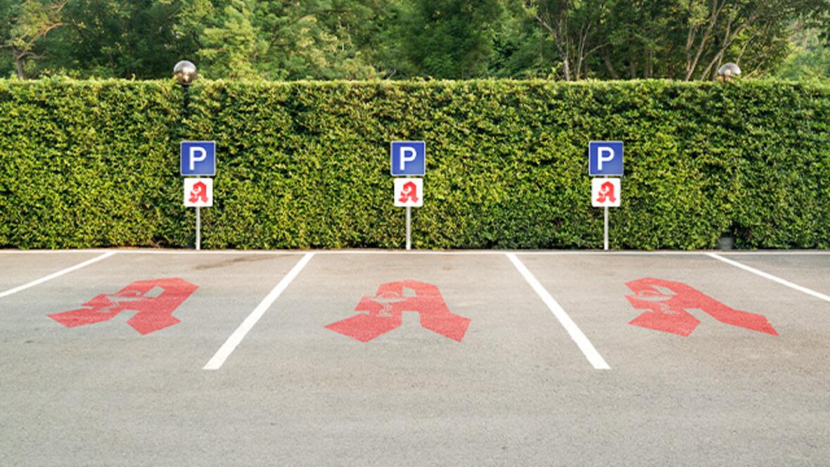 Drei gekennzeichnete kostenlose Apothekenparkplätze vor einer grünen Hecke.