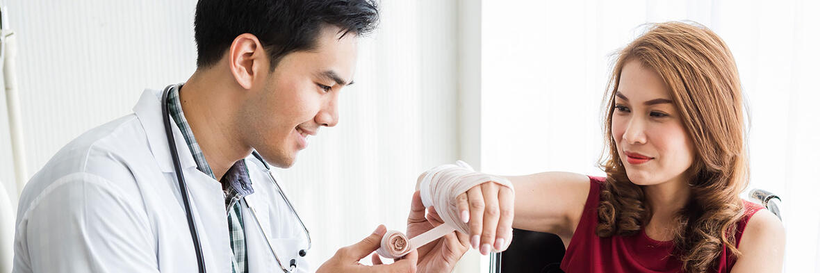 Ein Arzt legt einer Patientin einen Verband an der Hand an.
