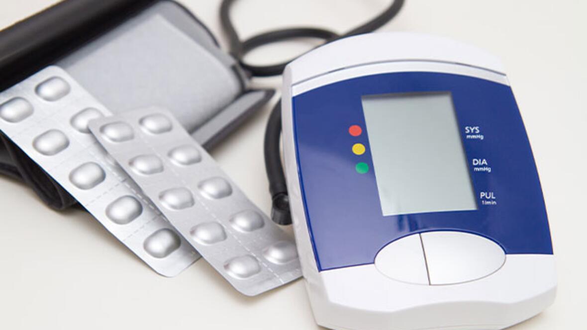 Digitales Blutdruckmessgerät mit Manschette neben mehreren Tablettenblistern.